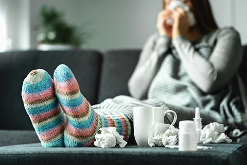 Syg dame i sofaen med uldsokker og snotklude