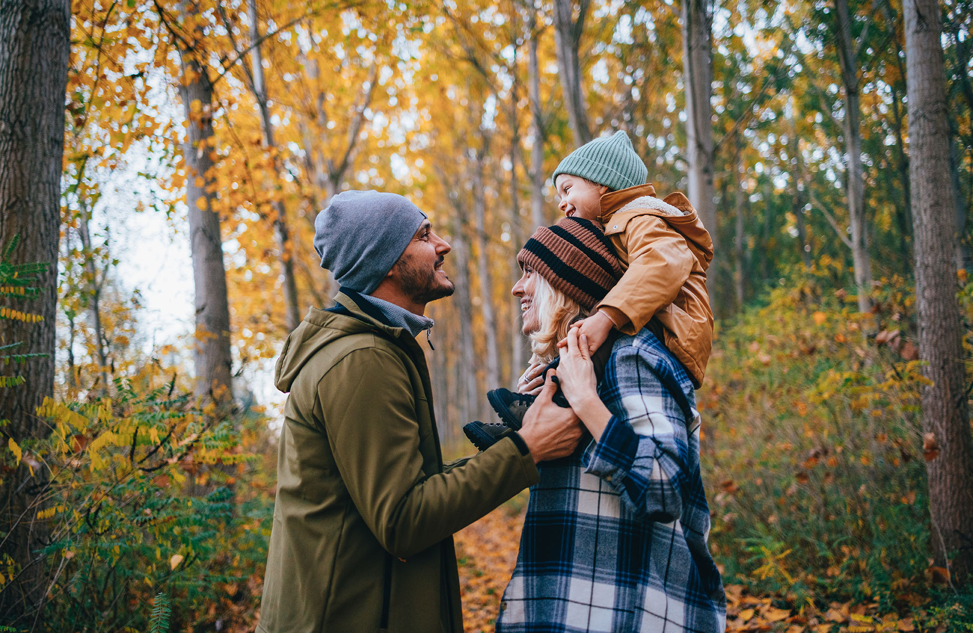 Mother, father, and child playing in the forest in autumn
